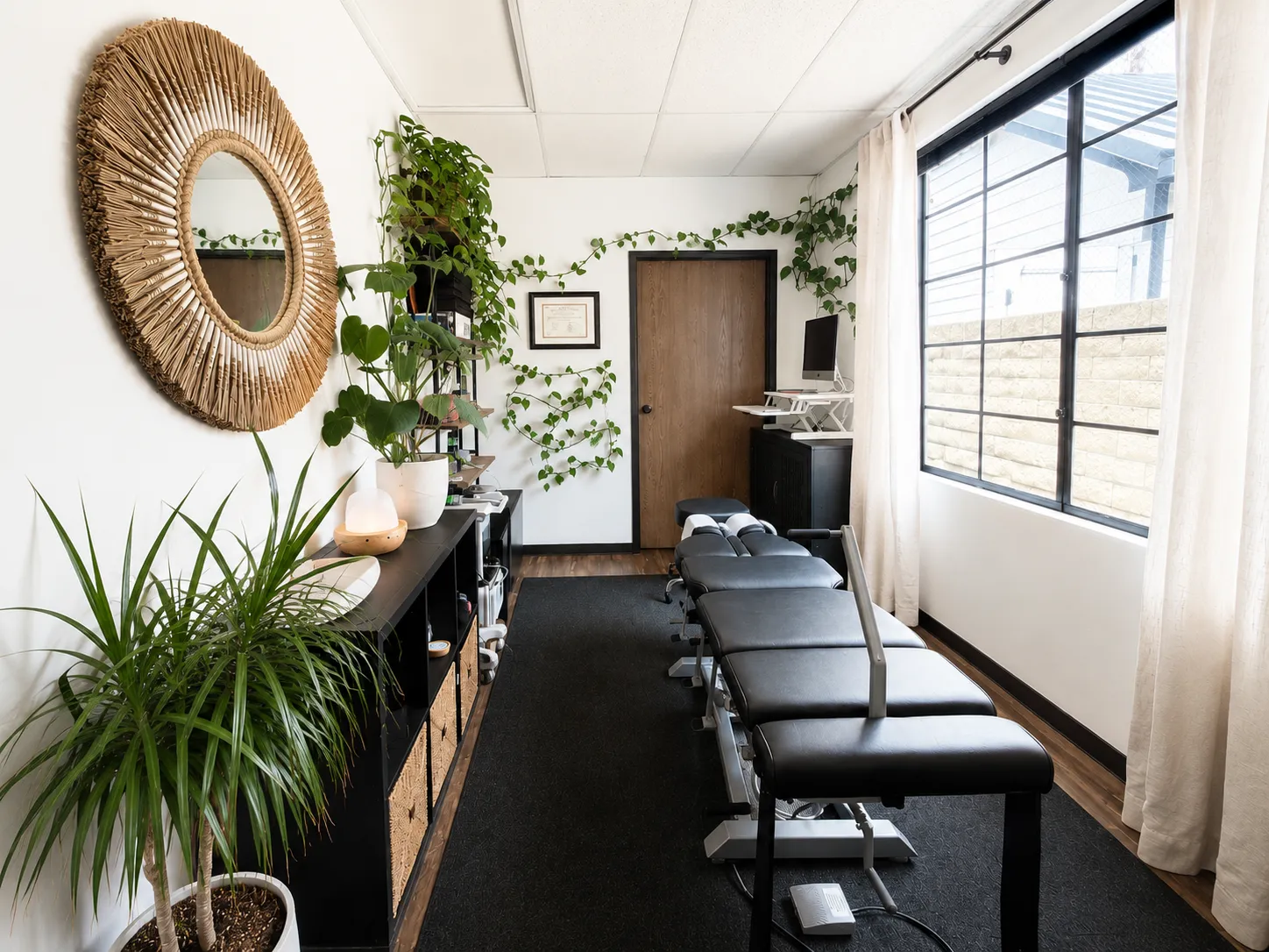The adjustment room at Huntington Beach Chiropractic, with a row of tables beside a curtained window and plants along the wall
